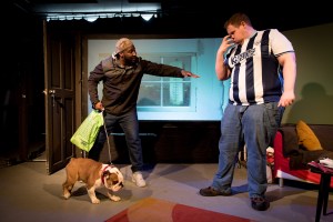 The man in the West Bromwich Albion shirt gestures with his hands putting a claw like muzzle to his face. Troy is trying to convince Bubble to take the dog.