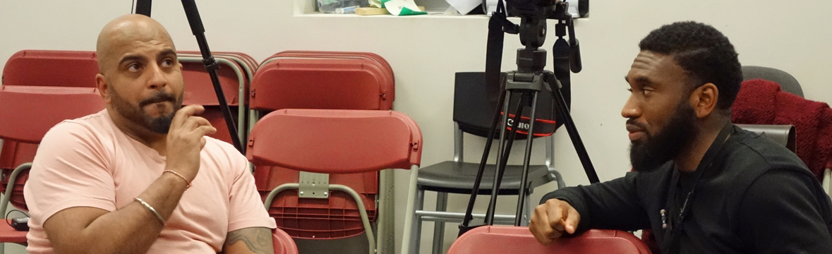 Two men sit in conversation in the seats where an audience sits